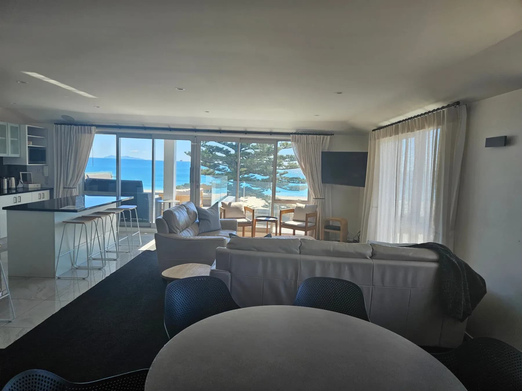 Open-plan lounge and kitchen with leather sofas and full ocean views through glass doors.