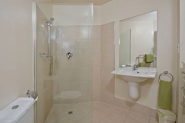 Bathroom with glass-enclosed shower, pedestal sink, mirror, and toilet.
