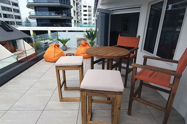 Rooftop balcony with wooden table, director's chairs, cushioned stools, and orange bean bags.