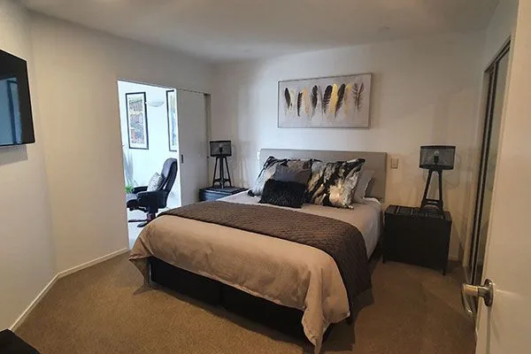 Bedroom with king bed, gray headboard, feather artwork, and adjoining office nook.