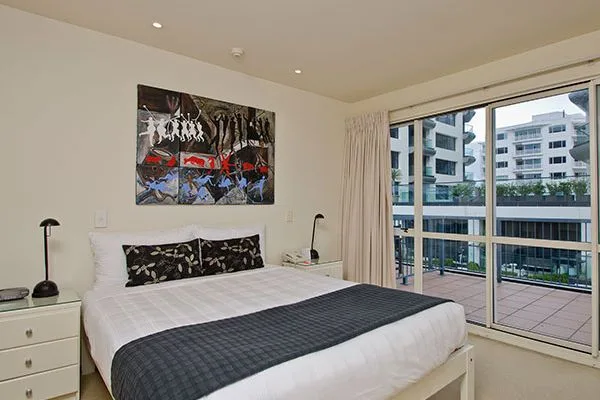 Bedroom with double bed, artwork, nightstands, and balcony overlooking nearby buildings.