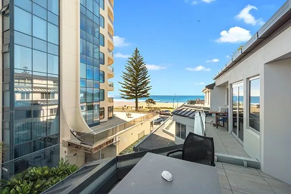Balcony view of a high-rise building, pine tree, and beach beyond.