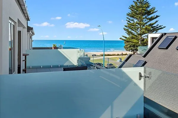 Ocean view from balcony with glass railings and rooftop solar panels visible.