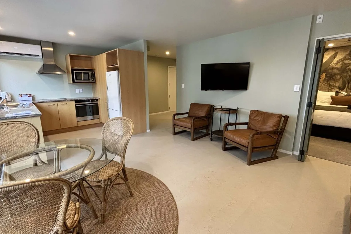 Open-plan living area with kitchen, dining table, leather armchairs, and wall-mounted TV.