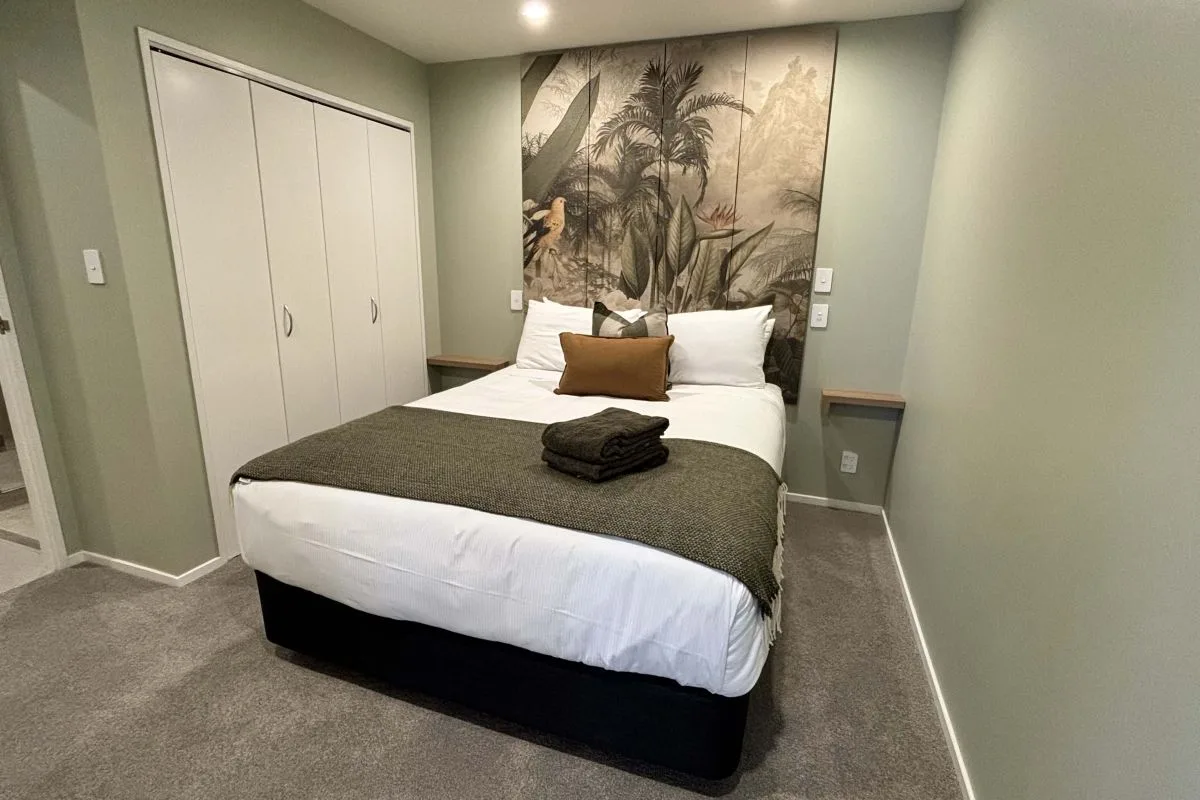 Bedroom with white built-in wardrobes, tropical wall mural, and folded throw blanket on bed.