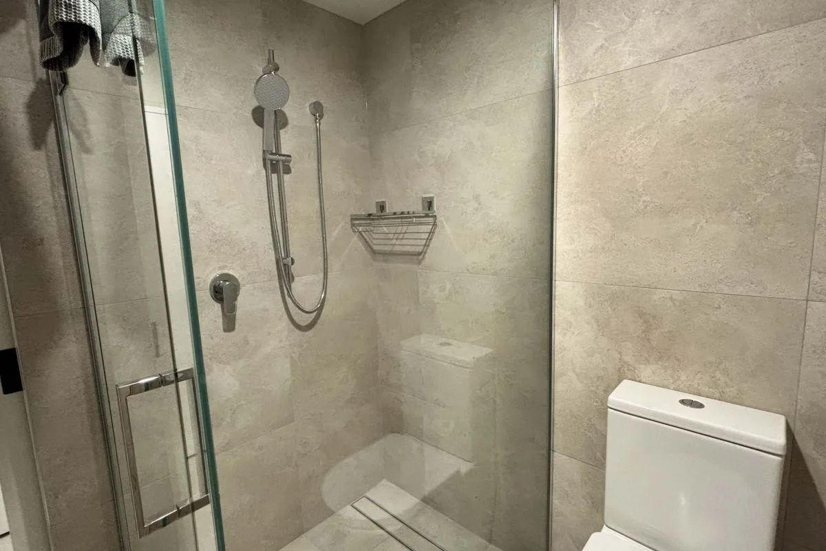 Bathroom with glass-enclosed shower, handheld showerhead, and toilet against tiled walls.